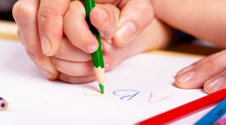 Child hand with pencil and woman hand helping to write letters