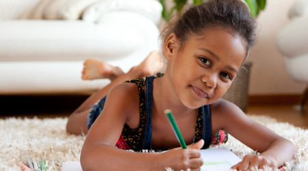 Little African Asian girl  drawing, lying down on the floor